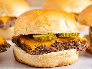 A tray of ovenbaked sliders with beef patties cheddar cheese and pickles in soft buns