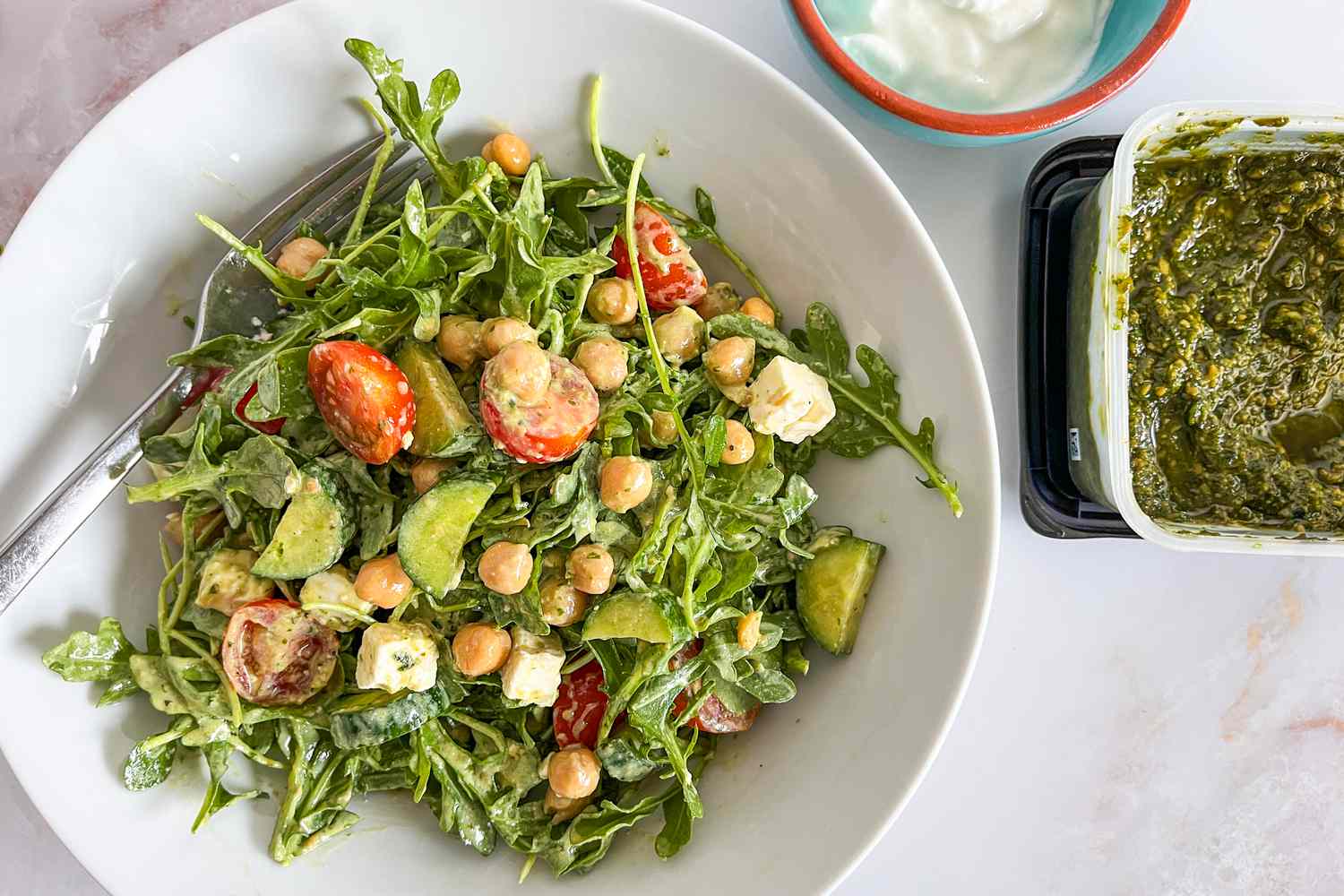 salad dressed with 2-ingredient salad dressing in a bowl next to a bowl of greek yogurt and a container of pesto