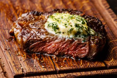 A grilled steak topped with herb butter on a wooden surface