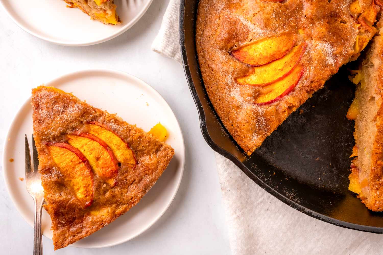 Slices of peach skillet cake on plates and in a cast iron pan served on a light background