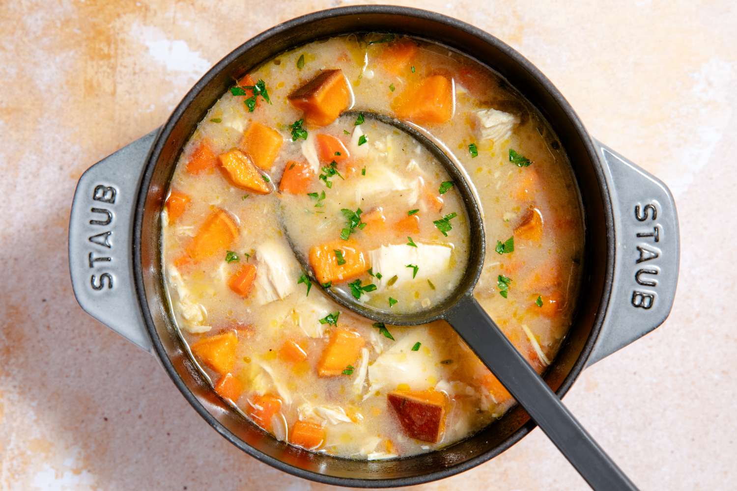 Overhead view of a gray dutch oven of chicken stew with a large serving spoon
