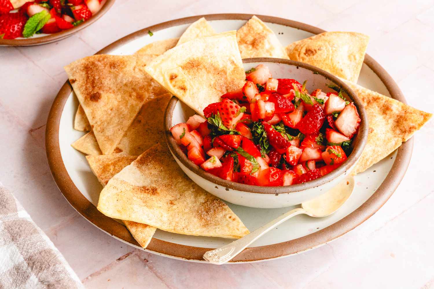 A bowl of strawberry salsa accompanied by tortilla chips on a plate