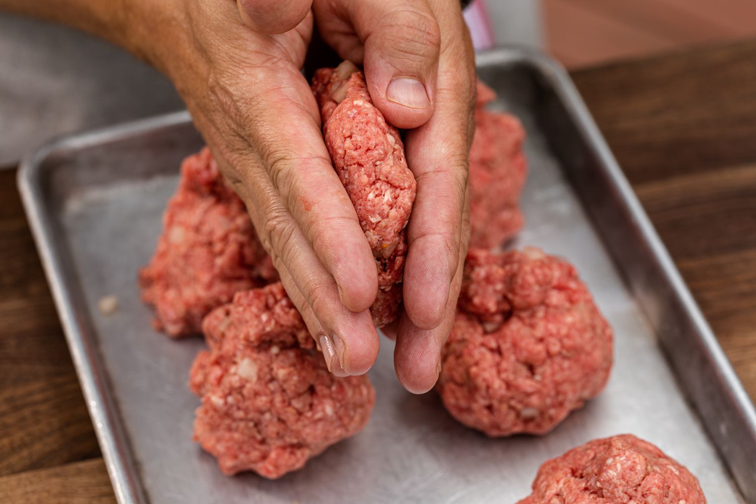 Hands flattening ground beef balls to make a classic bacon cheeseburger