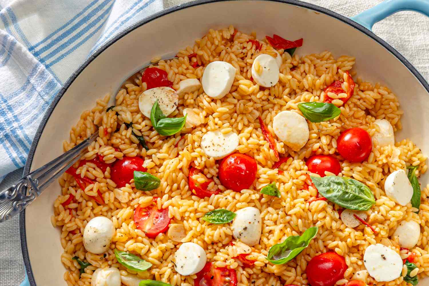 Caprese orzo with cherry tomatoes mozzarella and basil in a pan