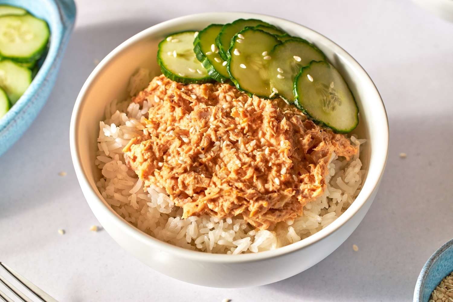 Spicy tuna and rice bowl topped with sliced cucumbers.