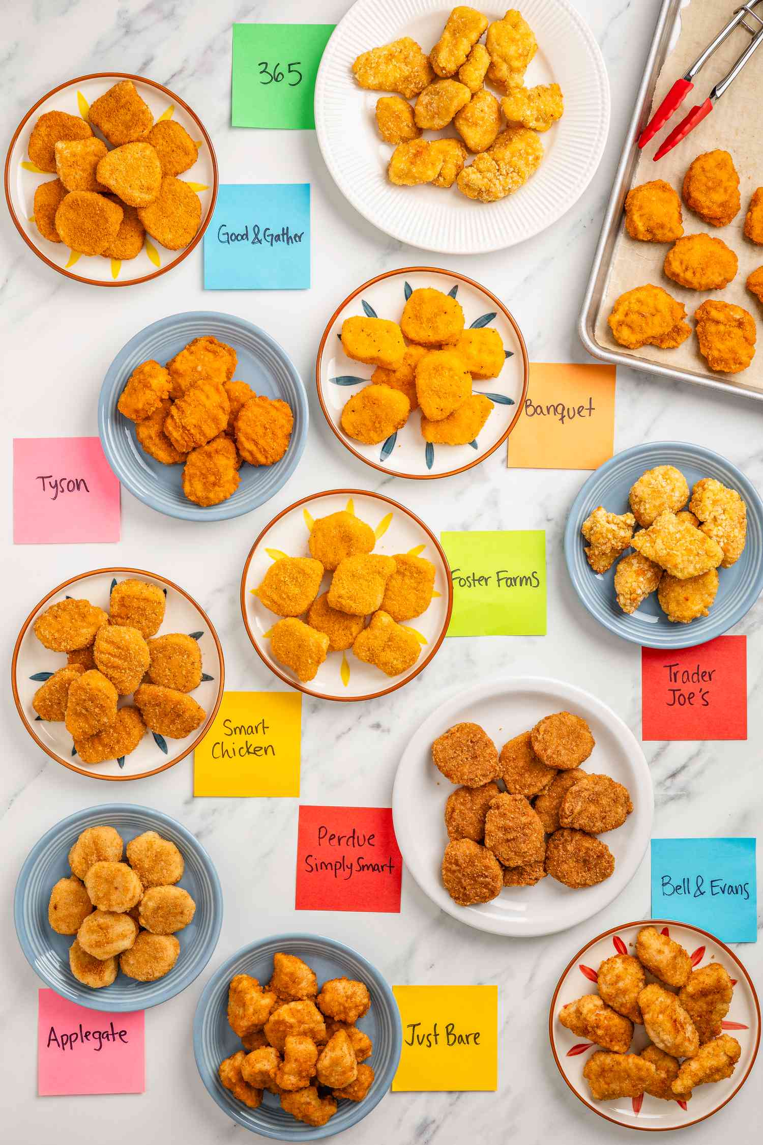 Different brands of chicken nuggets (each type of nugget on a plate with a sticky note next to each plate) and a baking tray with baked chicken nuggets