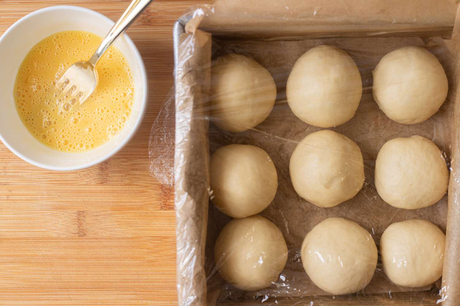 Rolls rising in a pan with butter next to it.