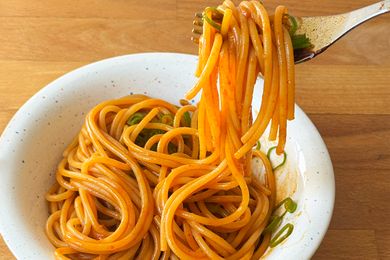 A bowl of cooked noodles being lifted by a fork garnished with green onion slices