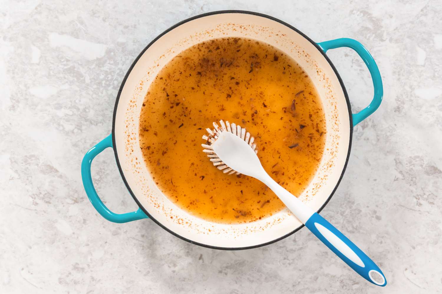 A pot with residual broth and a plastic spatula on a kitchen surface
