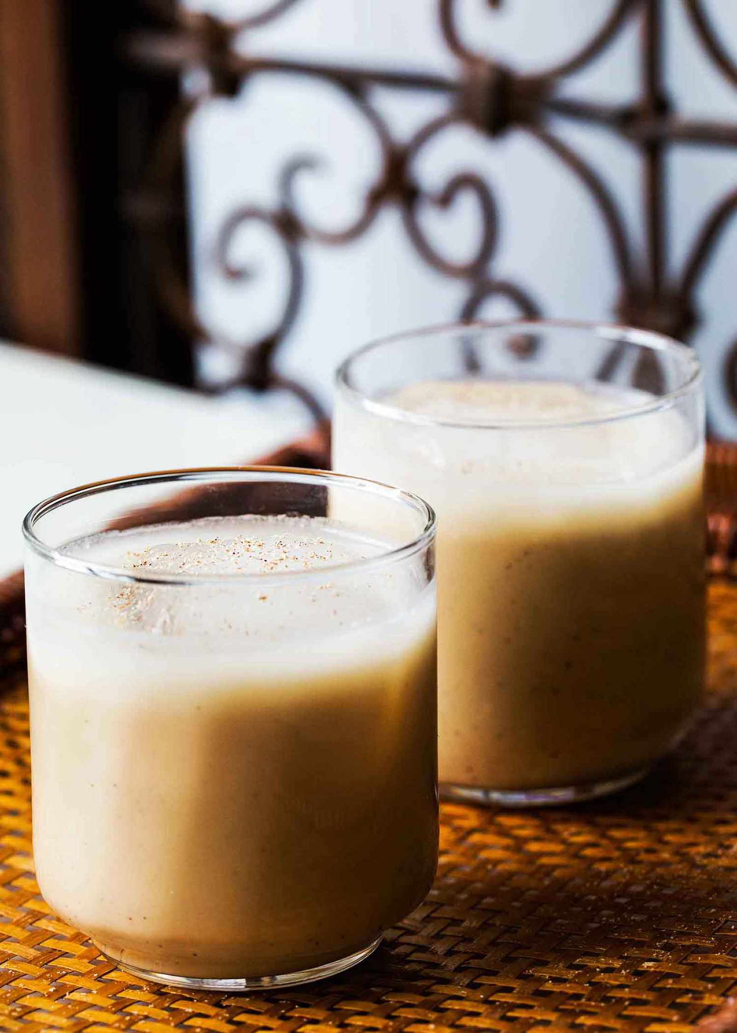 Two glasses of creamy Coquito on a woven mat