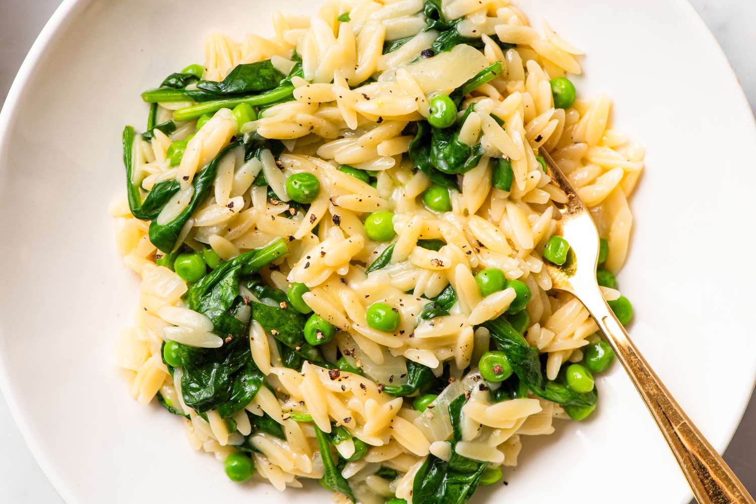 Orzo pasta with peas and greens on a plate with a fork