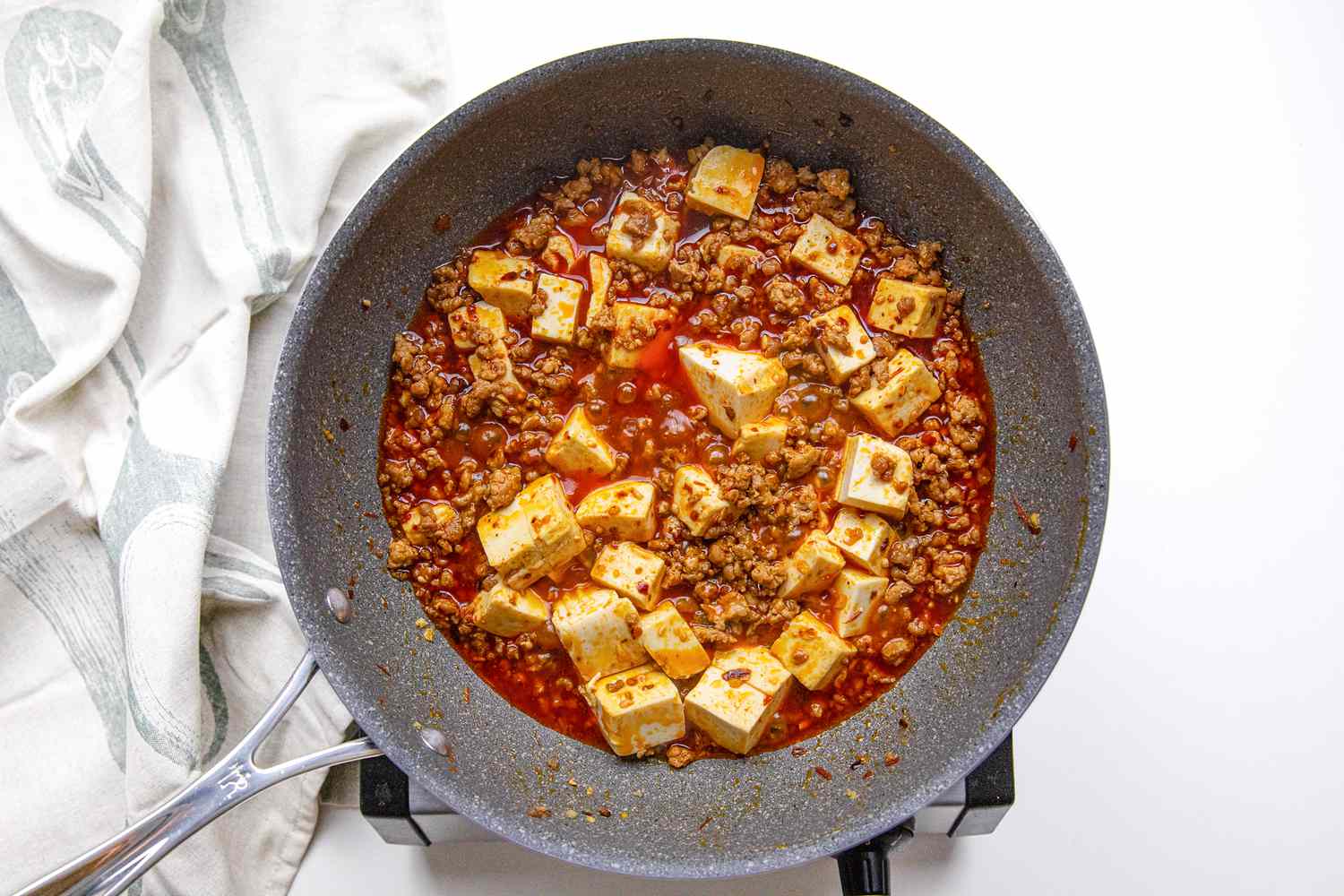 Mapo Tofu Simmering on the Portable Burner Next to a White Kitchen Towel After Cornstarch Slurry Was Added 