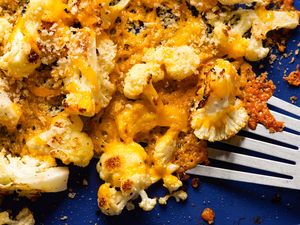 Roasted cauliflower topped with melted cheese and breadcrumbs with a fork on the side on a blue plate