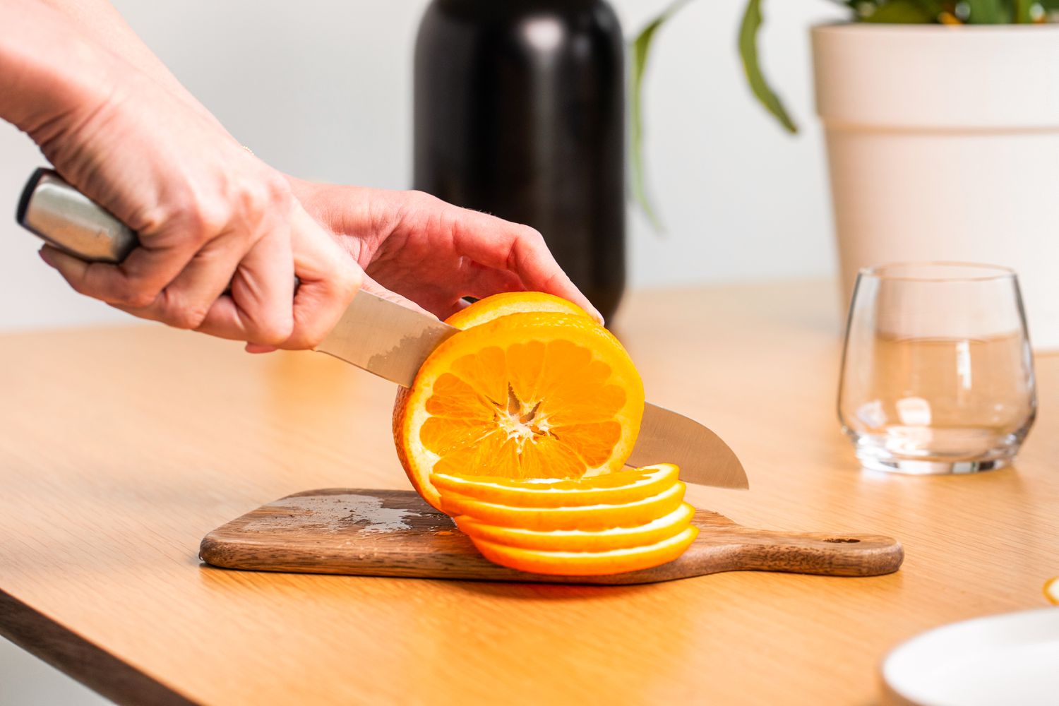 Someone cutting an orange with a knife on a small wooden cutting board