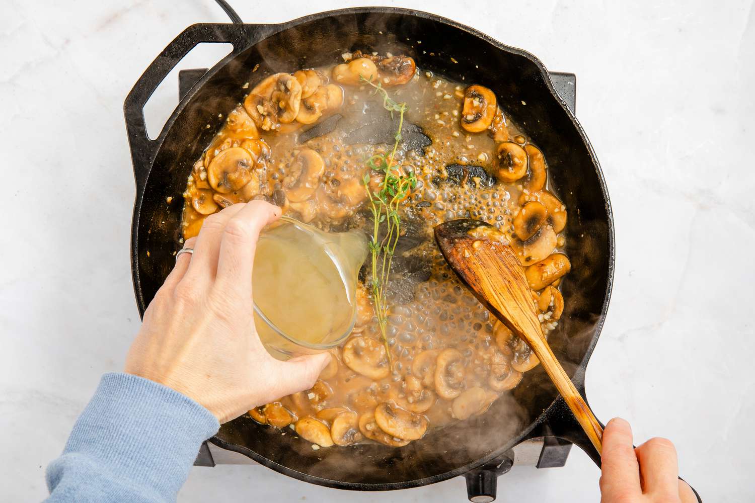 thyme and broth added to cast iron skillet for chicken marsala recipe