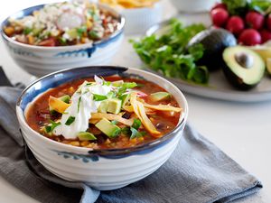 Meatless tortilla soup in a bowl topped with shredded cheese, sour cream, and tortilla strips.