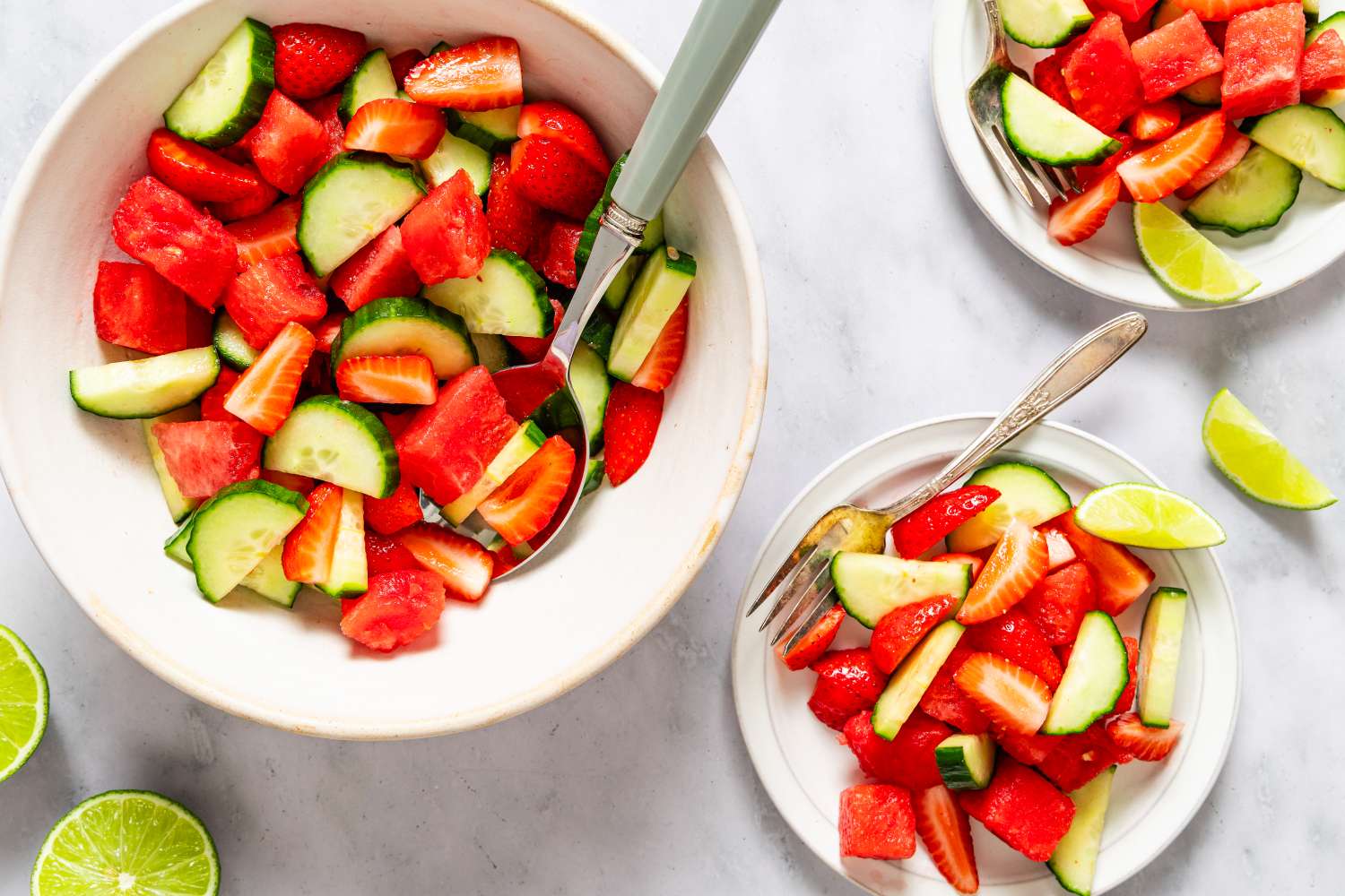 large bowl of Hydration Salad with a serving spoon, 2 small plates with a serving of the salad with a fork, lime wedges on the side