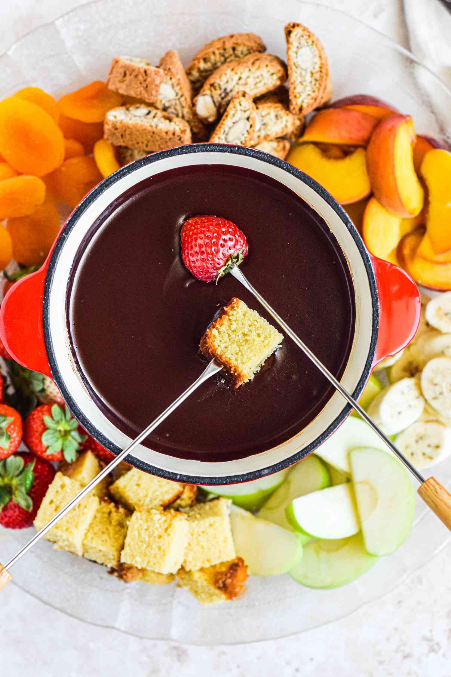 Dipping a strawberry and bread into fondue chocolate with other dippers surrounding.