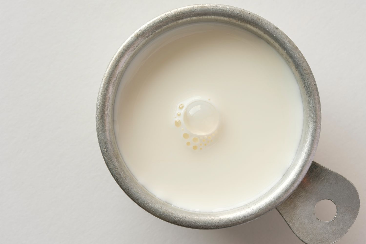 A small metal measuring cup filled with cream viewed from above