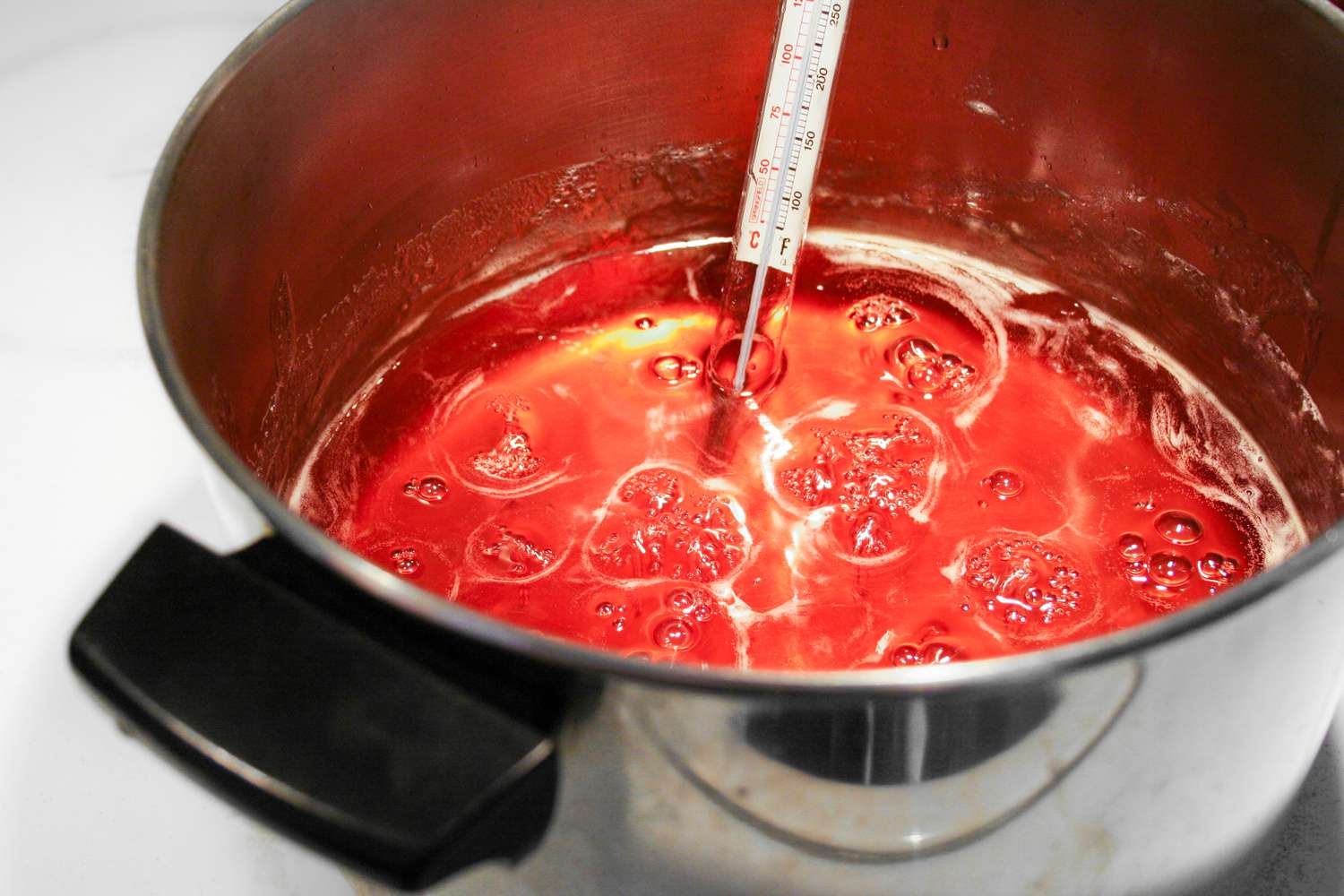 A pot of boiling quince jelly with a thermometer at the gelling point