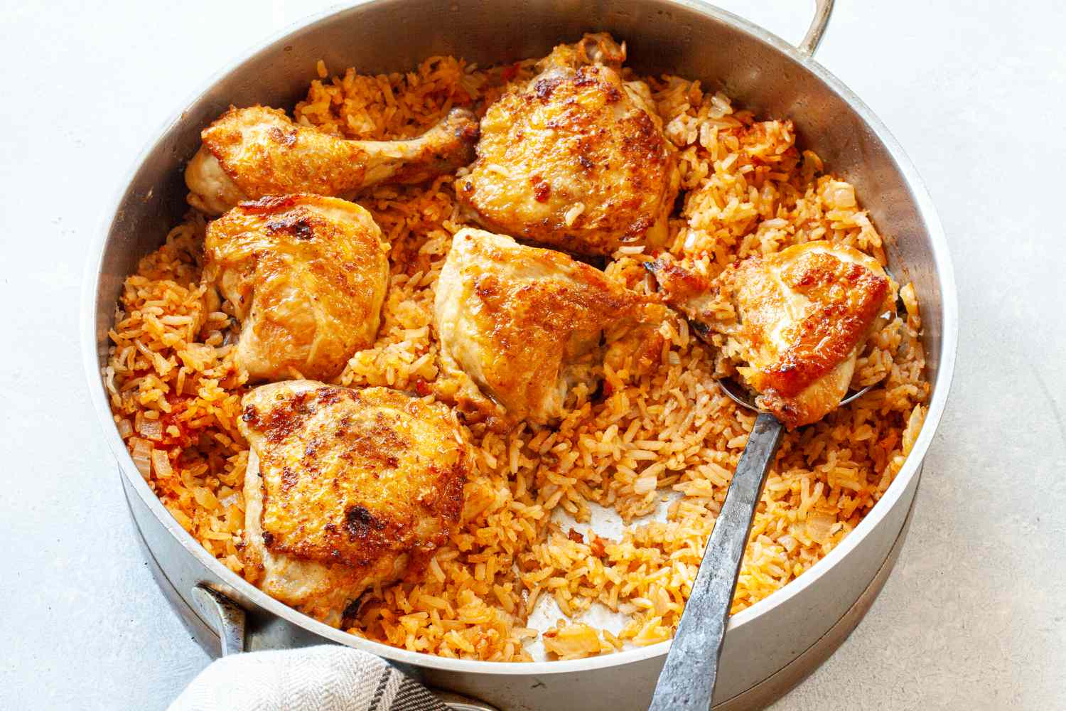 A deep skillet with arroz and a serving spoon.