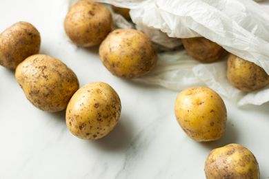 Overhead view of potatoes inside and outside a shopping bag on a marble countertop