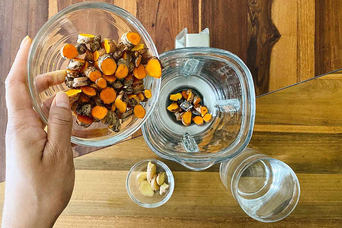 Chopped fresh turmeric being put in a blender to show how to make Jamu.