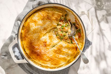 Overhead view of a dutch oven of weeknight chicken pot pie with a serving spoon all resting on a gray kitchen towel on a marble countertop