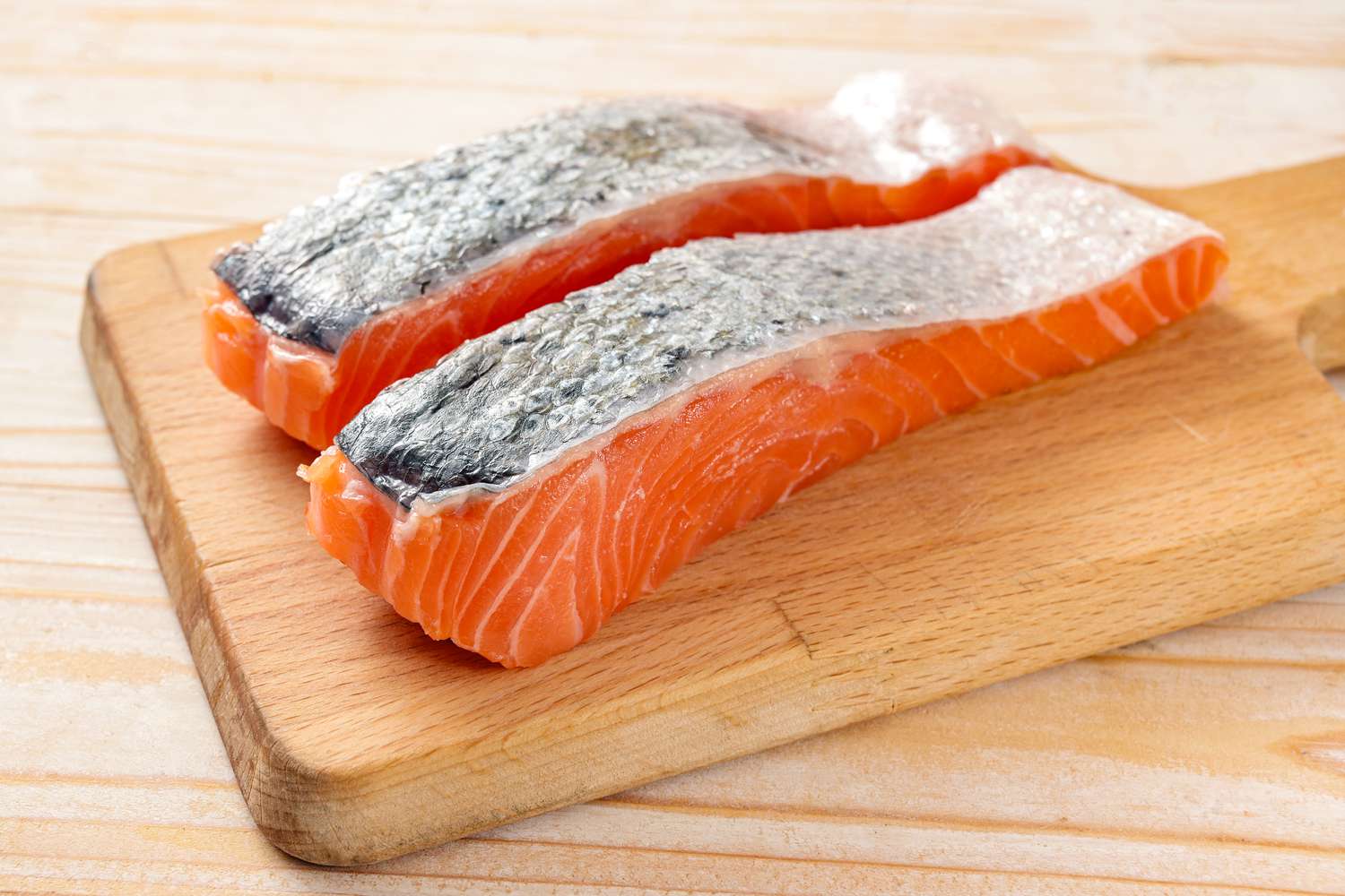 Side view of two skin-on salmon fillets on a wooden cutting board