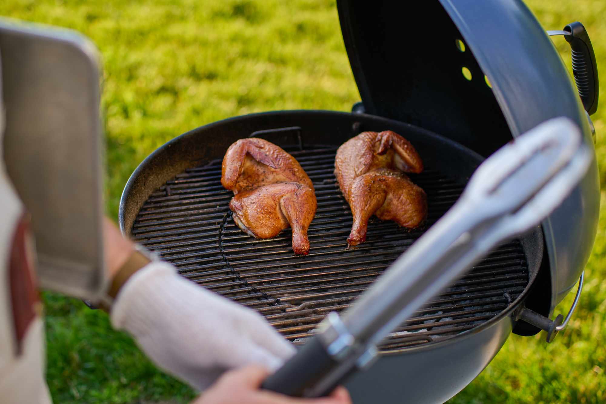 Two halves of grilled chicken on a round barbecue grill outdoors