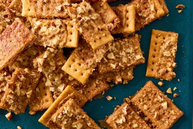 A pile of club crackers topped with crushed nuts on a teal background