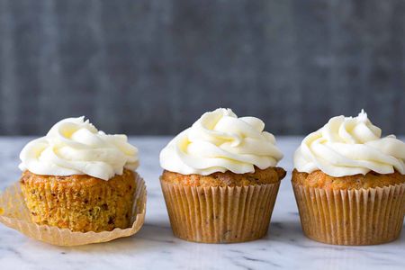 Three Carrot Cake Cupcakes topped with cream cheese frosting, one of them is partially unwrapped