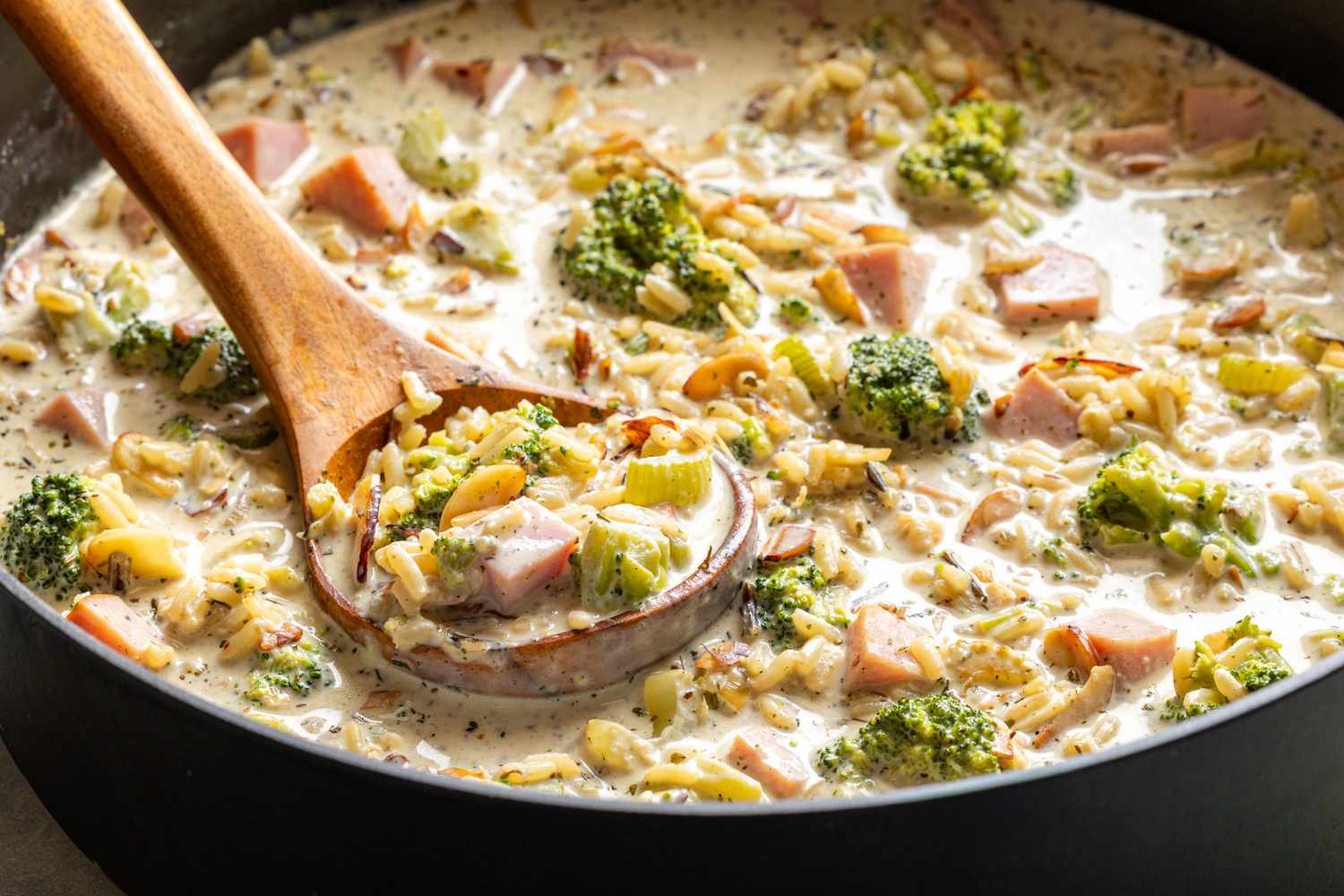 Creamy soup with broccoli wild rice ham and celery in a pot with a wooden ladle