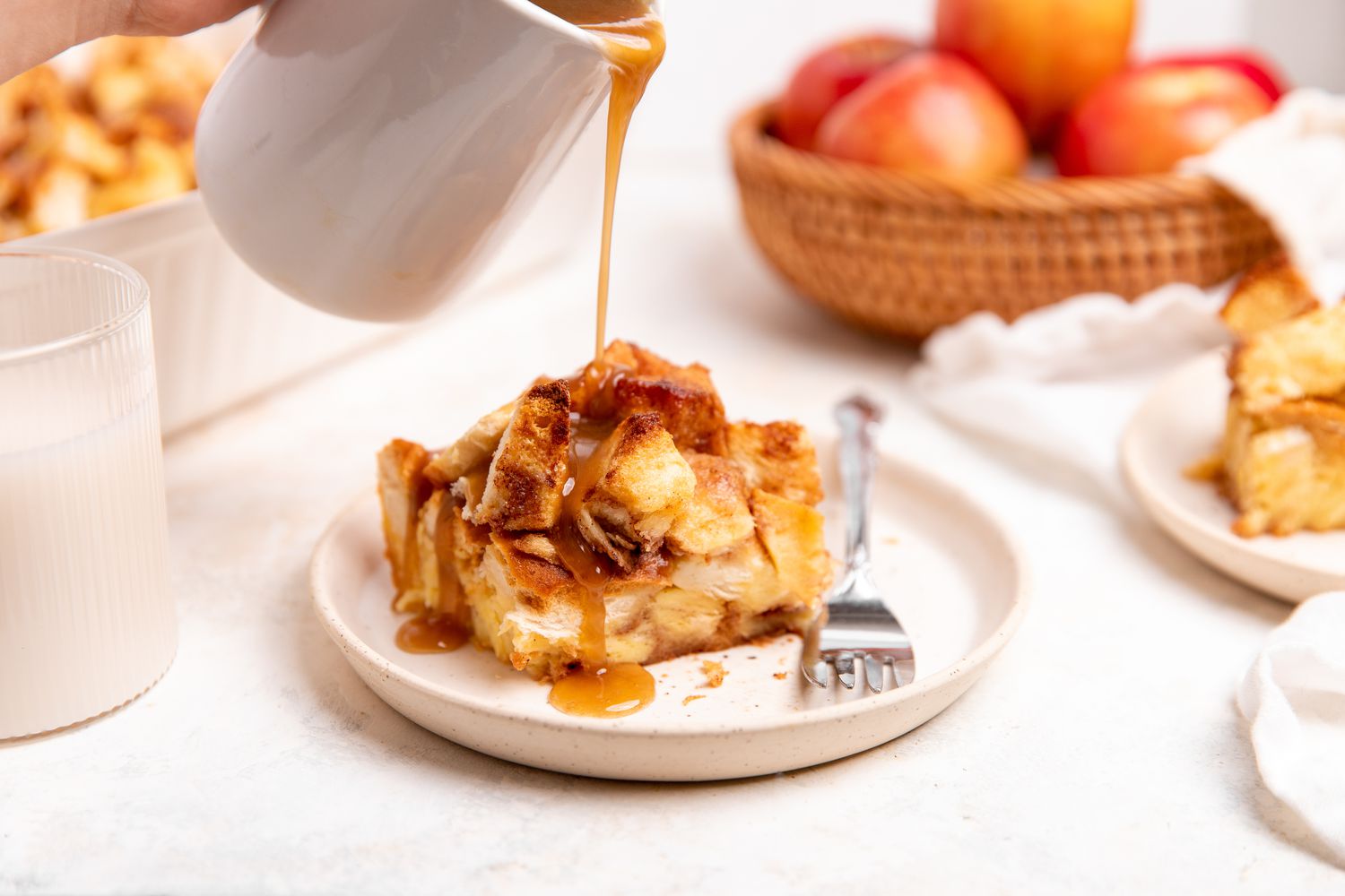 Slice 0f Apple Bread Pudding on a Plate with Sauce Drizzling from a Milk Pitcher