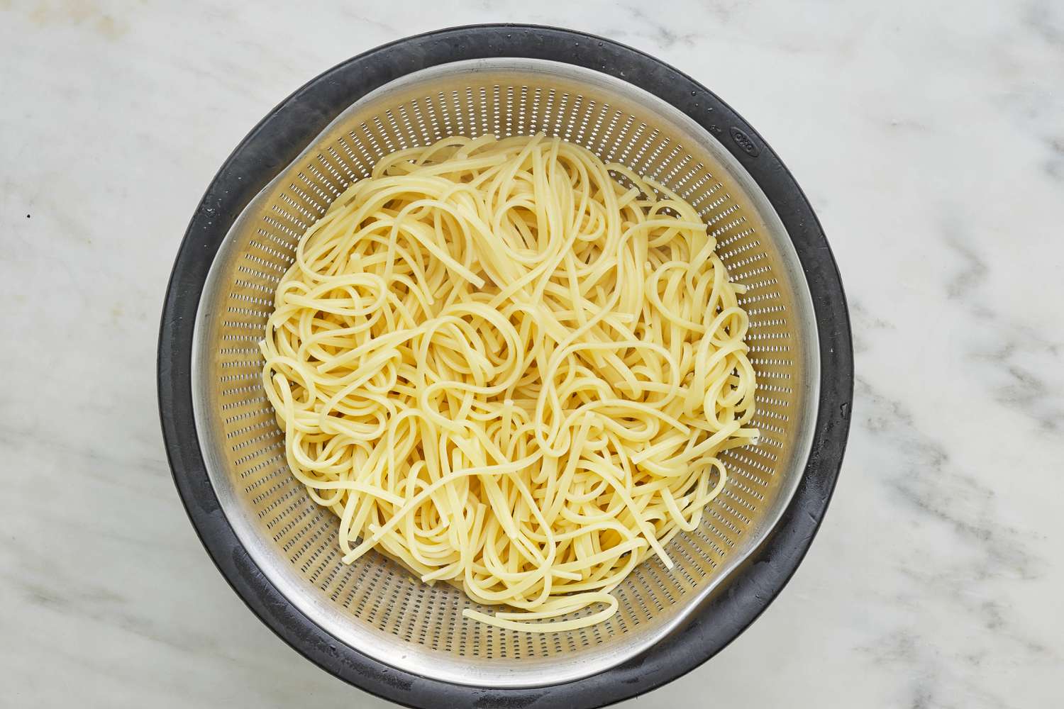 Cooked pasta in a colander over a bowl for linguine with tuna and capers recipe