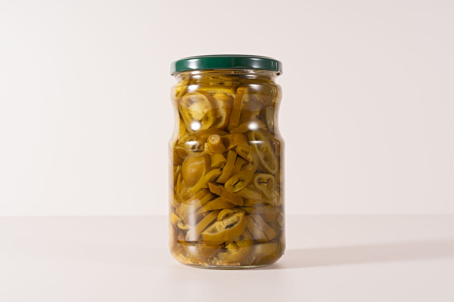 Jar filled with sliced pickled jalapeos on a plain surface