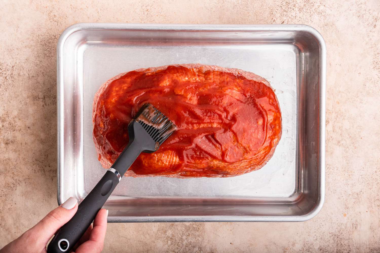 Ketchup Spread Onto the Meatloaf on the Baking Pan, Using a Silicone Basting Brush