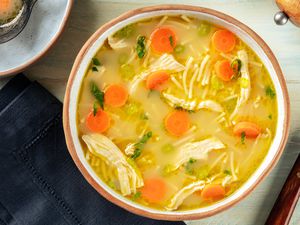 A photo of a bowl of chicken soup with carrot rounds and shredded chicken