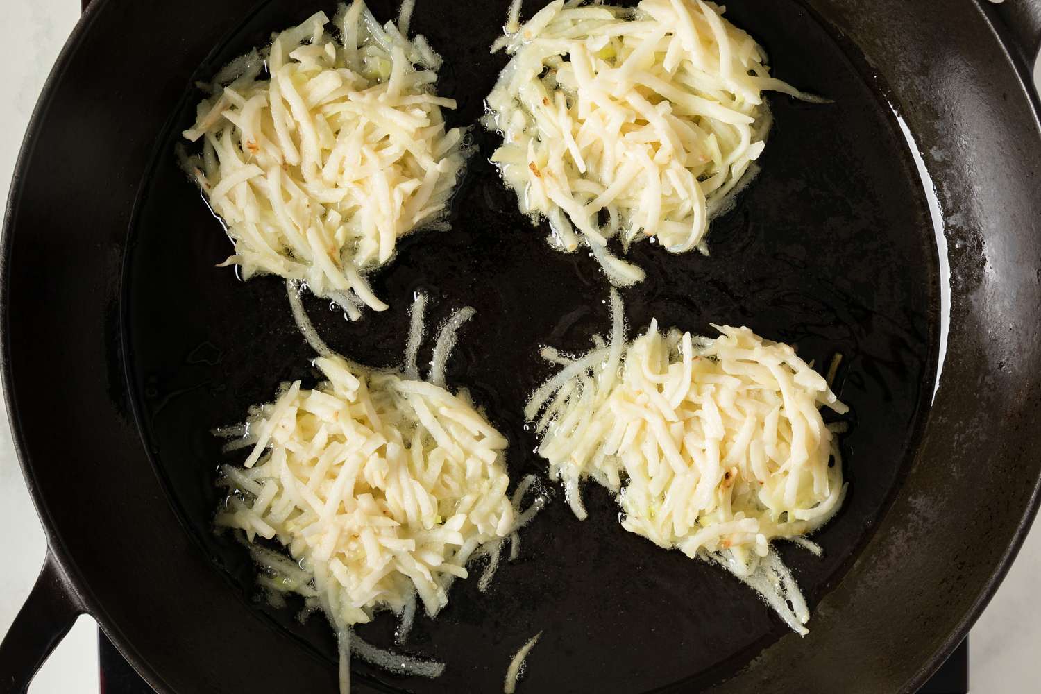 Four latke portions frying in a skillet