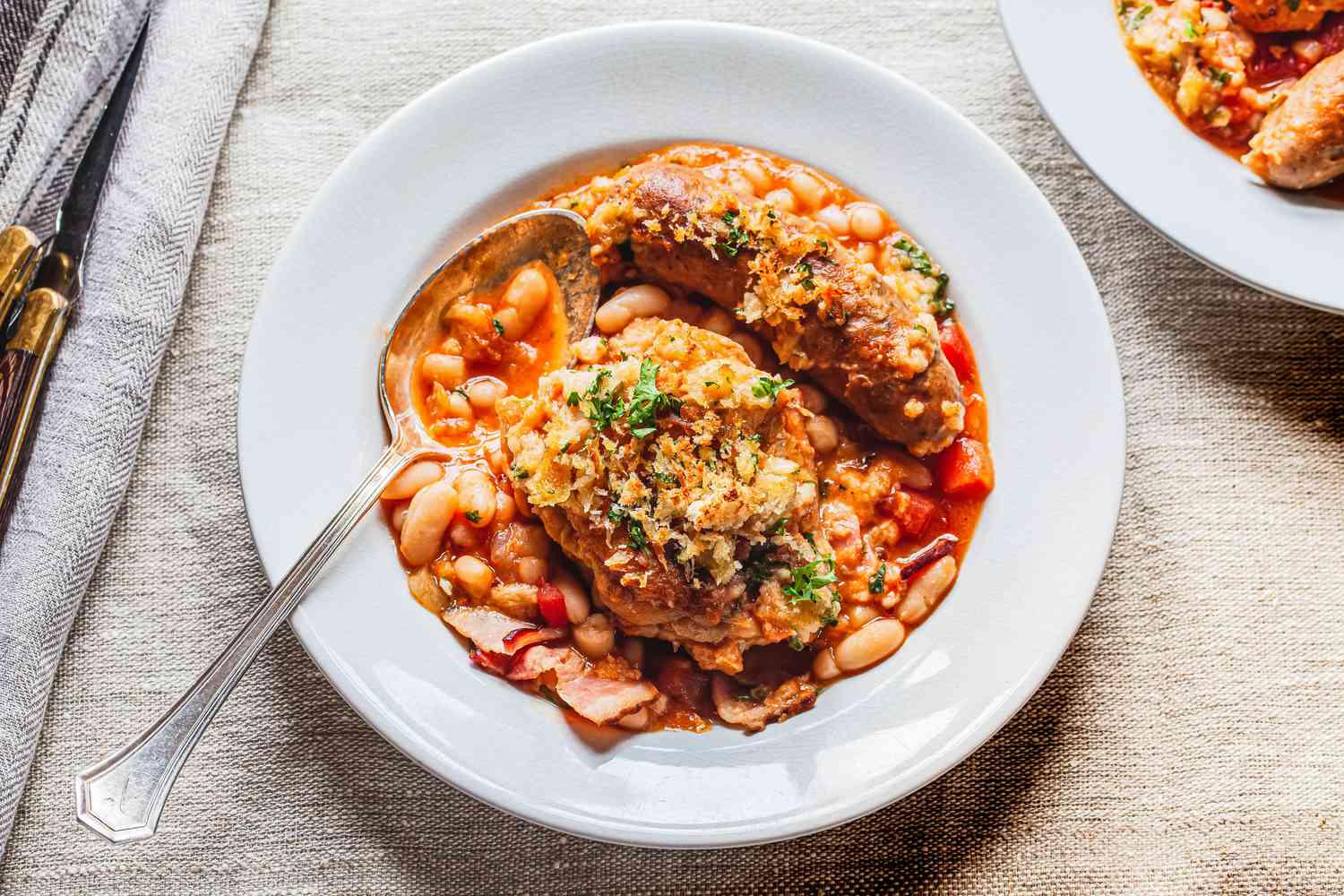 A white bowl of cassoulet with chicken and Italian sausage.