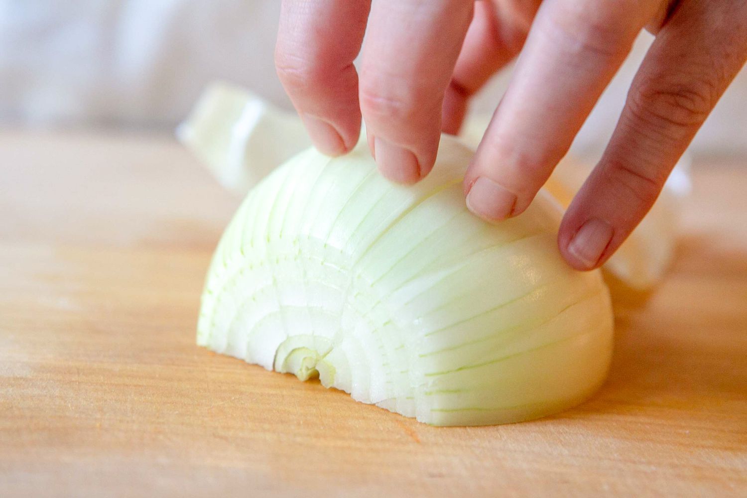 Curled Fingers Resting on Top of Sliced Onion for How to Chop an Onion