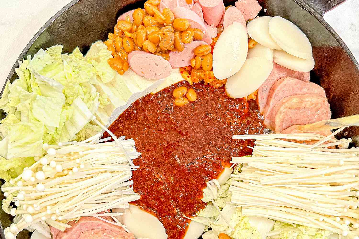 Budae jjigae (army base stew) ingredients beautifly organized around the perimeter of the pot and in the middle is the budae jjigae sauce