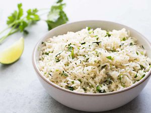 A bowl of cilantro lime rice with a cilantro and a lime wedge in the background