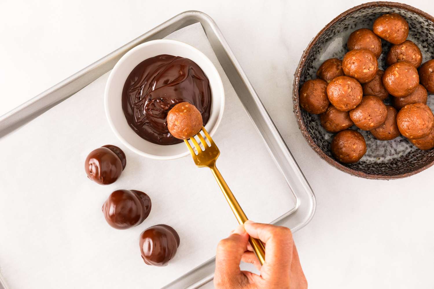Overhead view of a bowl of rum balls from Granny's Rum Balls recipe and a ball being dipped into chocolate with a fork and placing on a baking sheet with parchment paper
