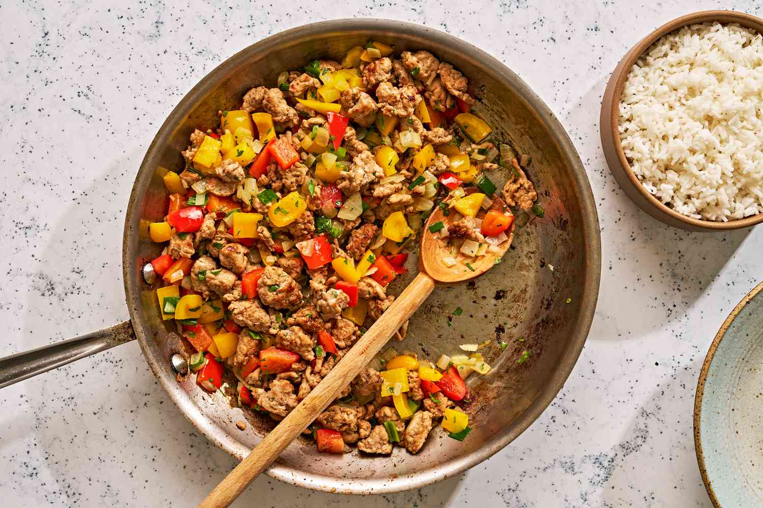 A skillet of cooked ground turkey and bell peppers on a counter with a bowl of white rice on the side