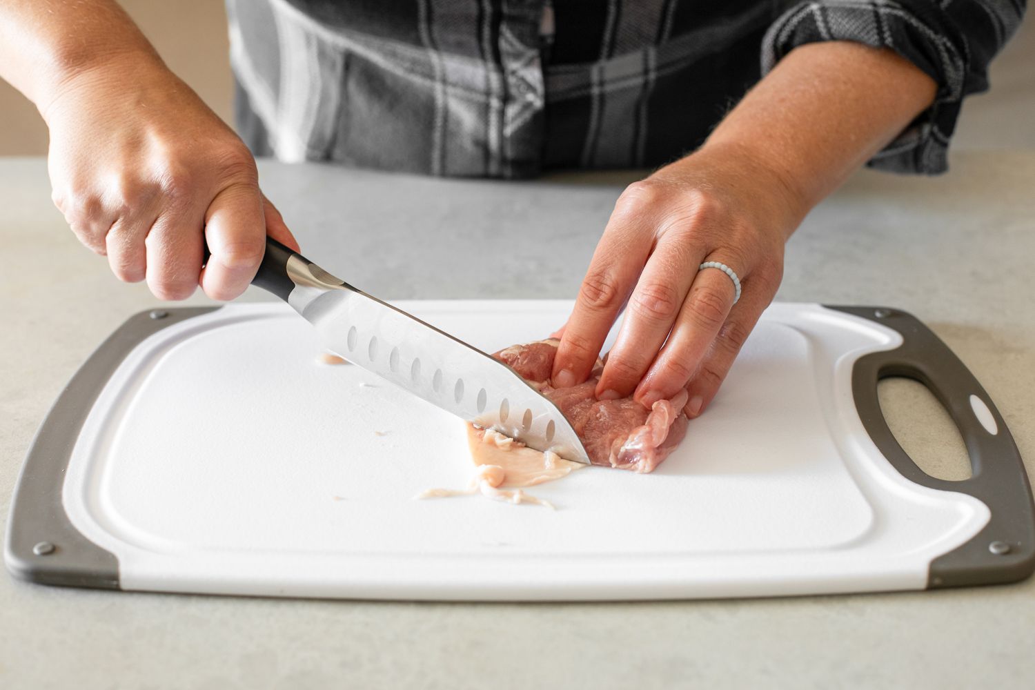 Knife Used to Remove Unwanted Trimmings from Chicken Thigh on a Cutting Board