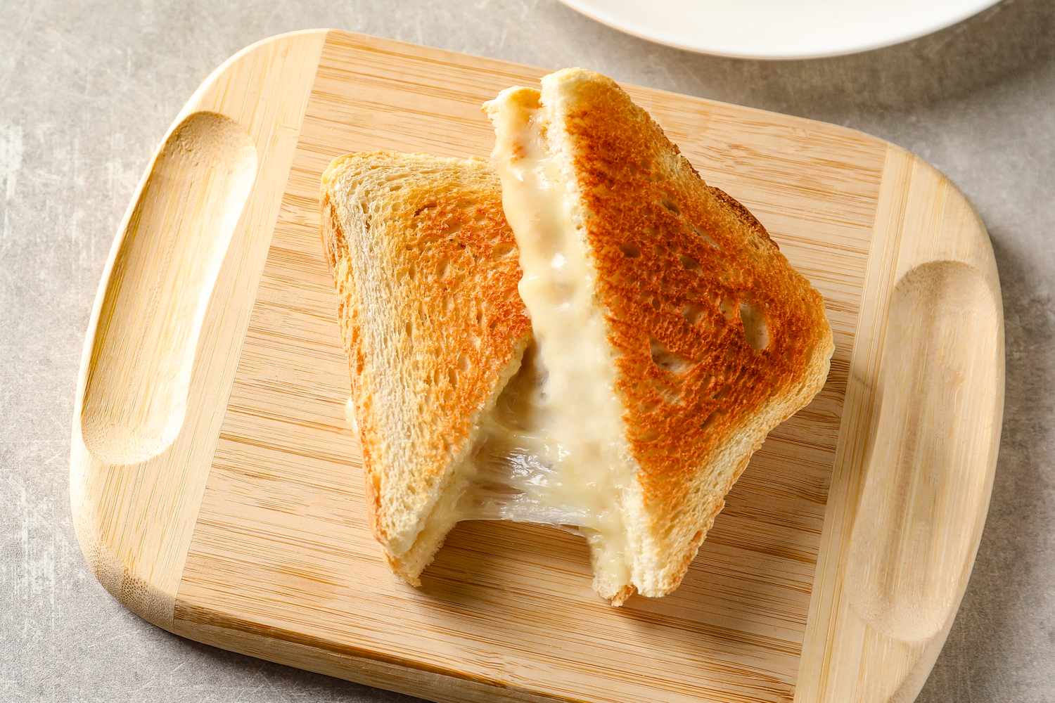 Grilled cheese sandwich on a wooden board cut into triangles with melted cheese oozing out