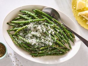 A dish of green beans topped with finely grated cheese served on a white oval plate with a spoon