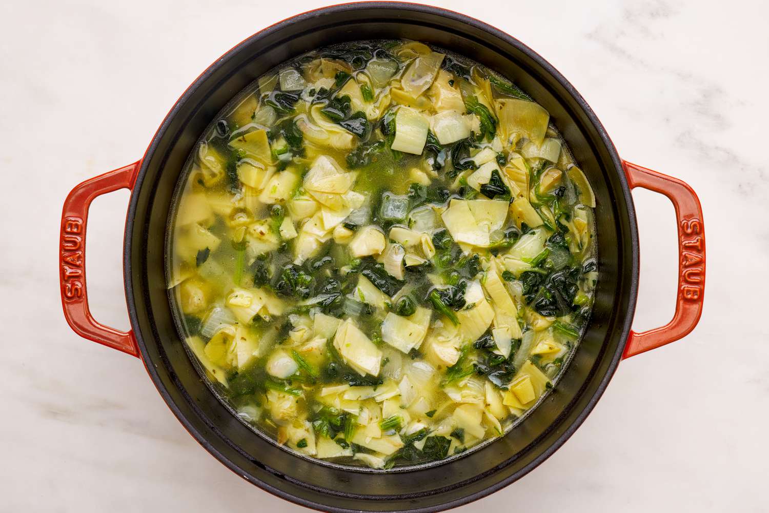 Spinach, artichoke hearts, and broth added to Dutch oven for spinach artichoke dip soup recipe