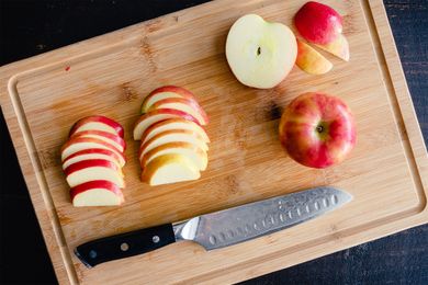 Sliced and whole apples on a cutting board with a knife placed nearby